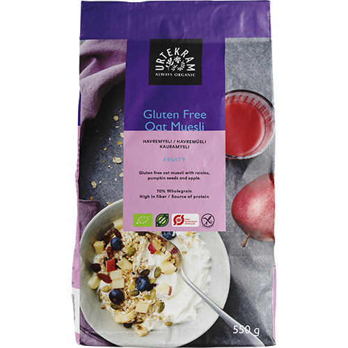 550 g:n pussi Urtekram Gluten Free Oat Muesli -myslia hedelmien kera, sisältää täysjyväkauraa ja kuvia myslistä kulhossa maidon, marjojen, pähkinöiden ja hedelmien kera, sekä lasillisen mehua ja päärynän. Pakkaus on mattapintaista muovia neutraaleissa sävyissä violetein tehostein. Tuotenimessä käytetään lihavoitua pääteviivatonta typografiaa etupuolella. Ihmisiä tai käsiä ei näy. Tausta on valkoinen ja tasaisesti valaistu.