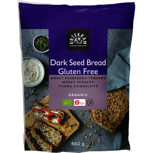 Urtekram Gluteeniton Luomu Tumma Siemenleipä Jauhoseos; pakkaus Urtekram Organic Gluten Free Dark Seed Bread -leipäjauhoseosta, 560 g; suorakulmainen paketti kiiltopäällysteisessä tummansinisessä muovipakkauksessa; etuosan kuvissa siemenleipäviipaleita, joista yhdessä tuorejuustoa, yrttejä ja tomaattia; tuotenimi lihavoidulla valkoisella kirjasimella; tausta tasainen, ei käsiä tai ihmisiä, studiokuva silmän korkeudelta.