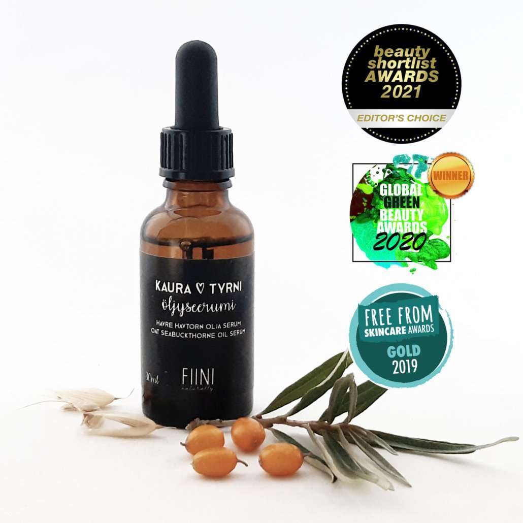 Fiini Naturally Kaura-Tyrni-Öljyseerumi; ruskea lasinen tiputinpullo mattapintaisena, valkoinen etiketti mustalla lihavoidulla groteskitekstillä "KAURA TYRNI eliyserum"; vierellä oransseja tyrnimarjatertut ja vihreitä lehtiä; oikealla puolella kolme pyöreää kauneus- ja ihonhoitopalkintomerkkiä pystysuunnassa; vaalea tausta.