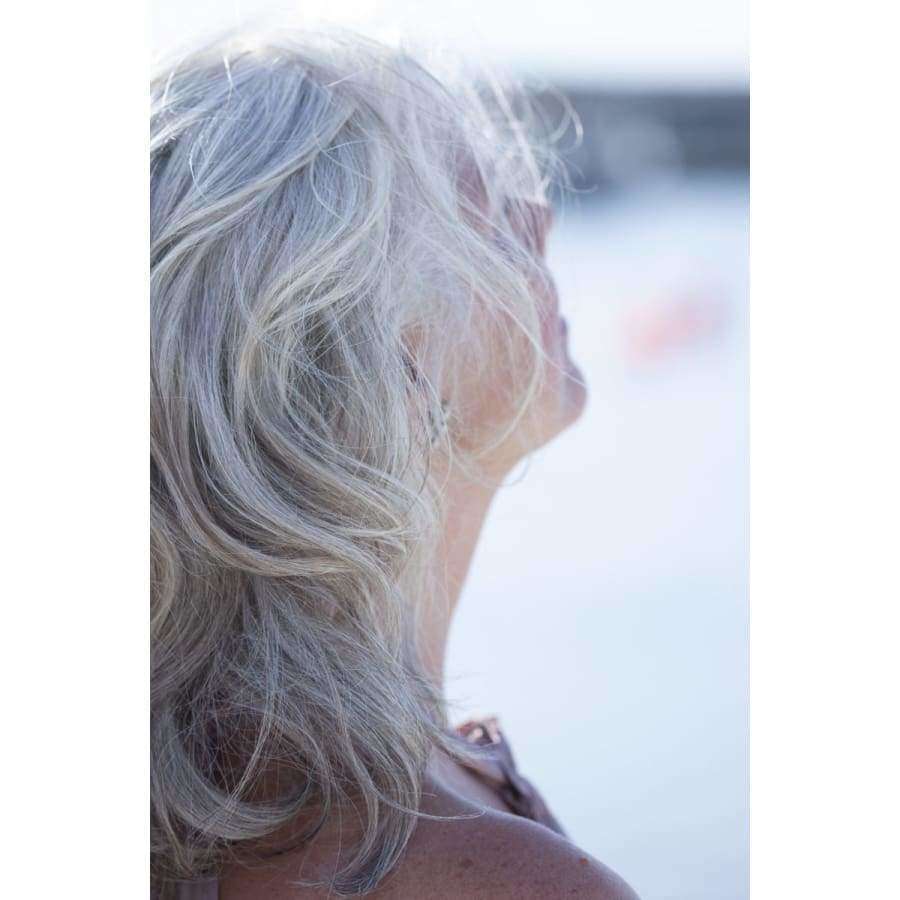 BRUNS Products Nº24 Blonde Beauty Hopeahoitoaine; nainen, jolla aaltoilevat harmaat hiukset, näkyy profiilissa kasvot poispäin kamerasta pehmeässä ulkovalossa; kasvot osittain hiusten peitossa; tausta sumennettu korostaen luonnollista vihreyttä; ei esineitä, pakkausta, etikettejä tai näkyvää tekstiä kuvassa; kuvatyyppi lähikuva muotokuva ulkotilassa.