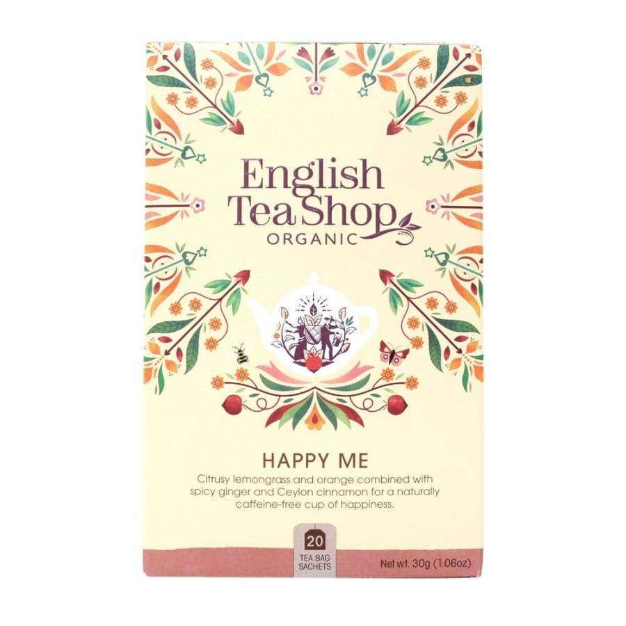 English Tea Shop Luomu Happy Me -teepakkaus; suorakulmainen ja mattapintainen rasia, pääväri turkoosinsininen, kuvituksena monivärisiä kukka- ja lehtikuvioita; valkoinen päätekirjasin, jossa käsialamaisia korostuksia; etiketti mainitsee 20 biohajoavaa teepussia sekä sitruunaruohon, appelsiinin, inkiväärin ja kanelin; kuvattu valkoista taustaa vasten, ei ihmisiä näkyvissä.