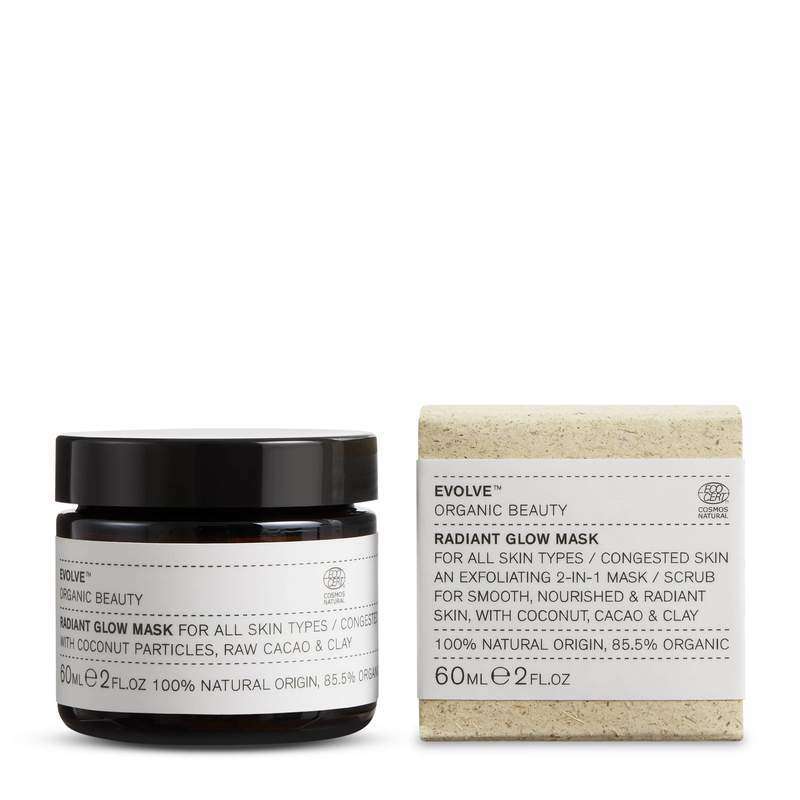 Evolve Radiant Glow Kasvonaamio -purkki ja pakkaus; musta, sylinterimäinen purkki valkoisella mattapintaisella etiketillä sekä vaaleanbeige suorakulmainen pakkaus; molemmissa yksinkertaista mustaa tekstausvapaata tekstiä; ainesosina mainittu kookoshiukkaset, raakakaakao ja savi; kuvattu yksiväristä taustaa vasten, ei ihmisiä tai käsiä näkyvissä.