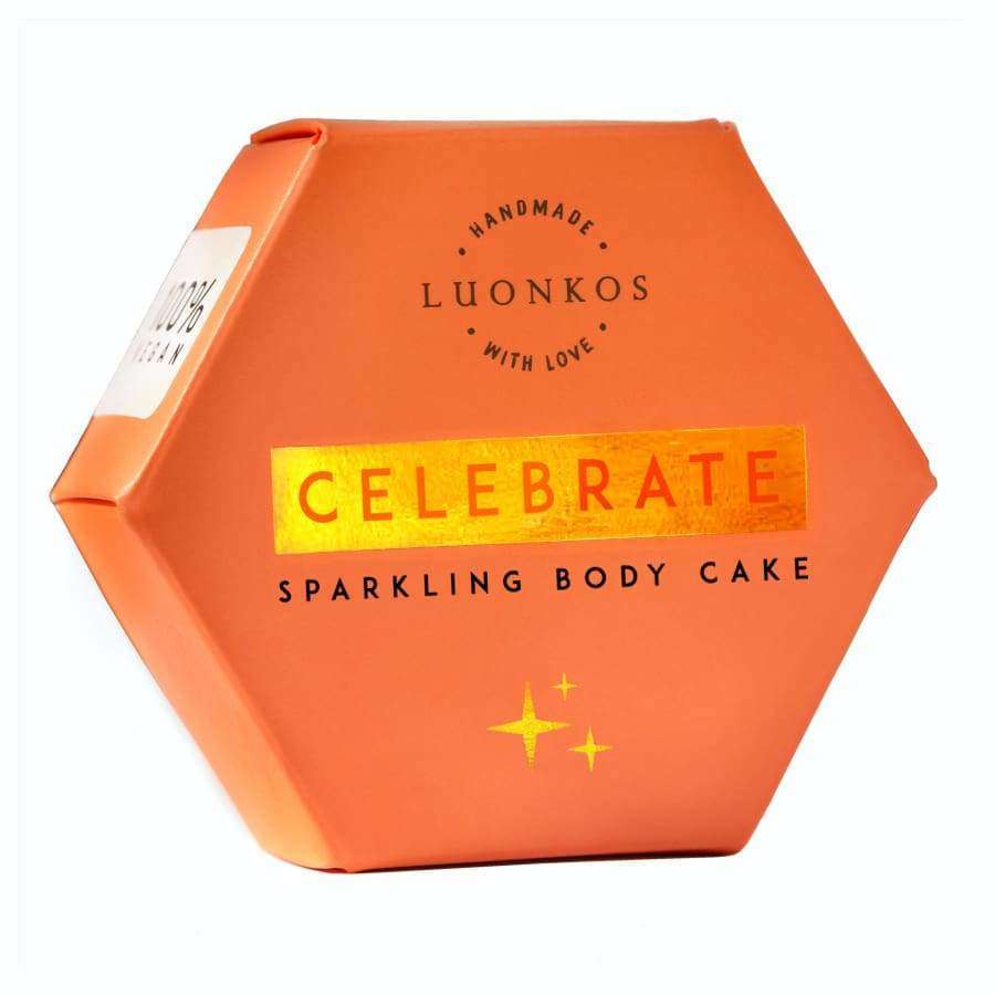 LUONKOS Celebrate Sparkling Body Cake, teksti "Handmade with love"; oranssi kuusikulmainen rasia kultaisin korostuksin ja ylellisin kimalluksin; sivut mattapintaiset, kultaiset metalliset yksityiskohdat; pääteksti lihavoidulla groteskifontilla, "Handmade with love" käsialatyylisellä fontilla; tuote kuvattu vaalealla taustalla, ei ihmisiä tai esineitä.