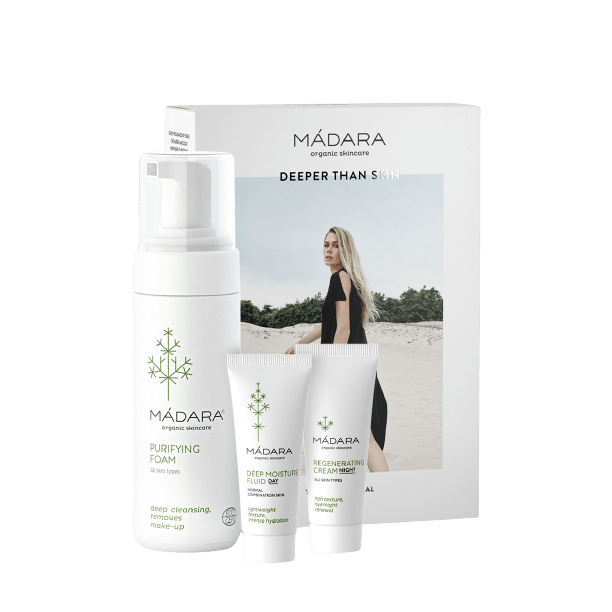 MÁDARA-ihonhoitosetti, sisältäen Purifying Foam-, Deep Moisture Fluid- ja Regenerating Cream -tuotteet, aseteltu pystyyn pahvirasian eteen. Astiat ovat valkoisia ja lieriömäisiä mattapinnalla ja minimalistisin mustin pääteviivattomin tekstein. Pakkauksessa on kuva mustapukuisesta naisesta seisomassa hiekkarannalla pilvisen taivaan alla.
