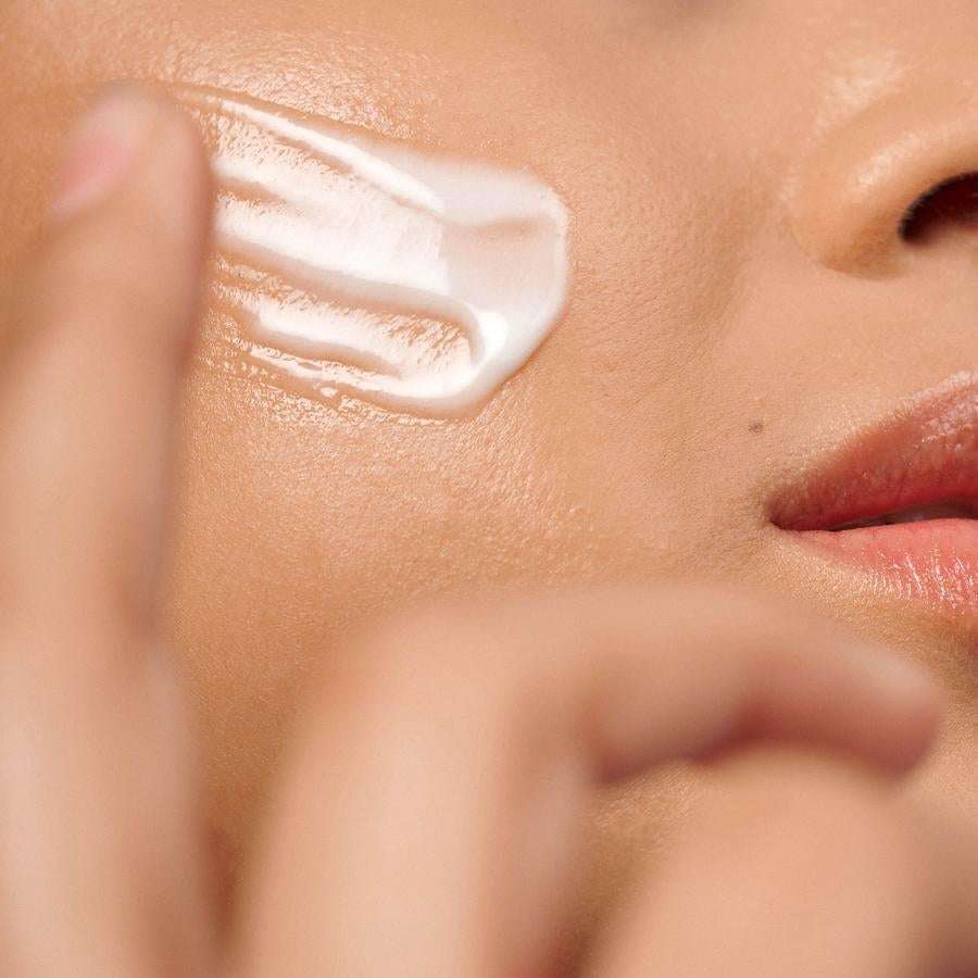 Novexpert HYALURONIC The Repulp Cream; lähikuva henkilöstä levittämässä valkoisen kosteusvoiteen raitaa poskelleen sormin, näkyvissä osa huulista; iho tasasävyinen ja hieman kiiltävä; kuvassa vain yhden käden sormenpäät toiminnassa; tausta pehmeästi epätarkka ja neutraali; ei pakkausta tai etikettejä näkyvissä.