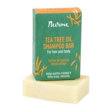 Nurme Tea Tree Oil Shampoo Bar -laatikko, vihreä ja keltainen, seisoo luonnonvalkoisen suorakulmaisen shampoopalan takana; laatikko mattapintaista pahvia lohkokirjaimin ja yksinkertaisin ikonikorostuksin; molemmat esineet vaaleaa yksinkertaista taustaa vasten; ei ihmisiä tai rekvisiittaa näkyvissä tässä tuotekuvassa.
