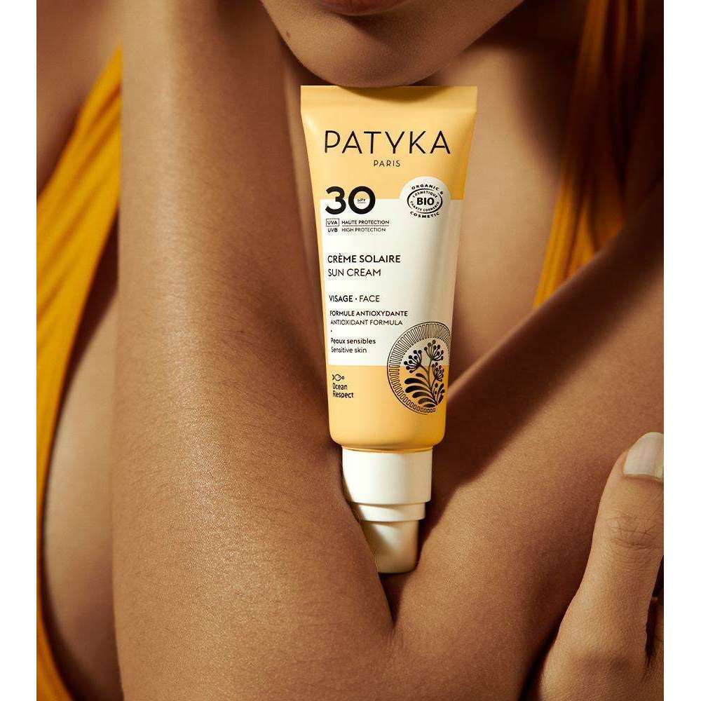 Patyka Face Sun Cream SPF30 Aurinkovoide kasvoille; keltaiseen vaatteeseen pukeutunut henkilö pitelee Patyka Paris SPF 30 -aurinkovoidetuubia rintansa edessä; tuubi muovia, pääosin keltainen ja valkoinen mattapinta yksinkertaisin mustin kirjaimin; tuotetiedot, mukaan lukien "Patyka Paris" ja "SPF 30", painettu etuosaan; tausta ja muut yksityiskohdat eivät näy rajatussa kuvassa.