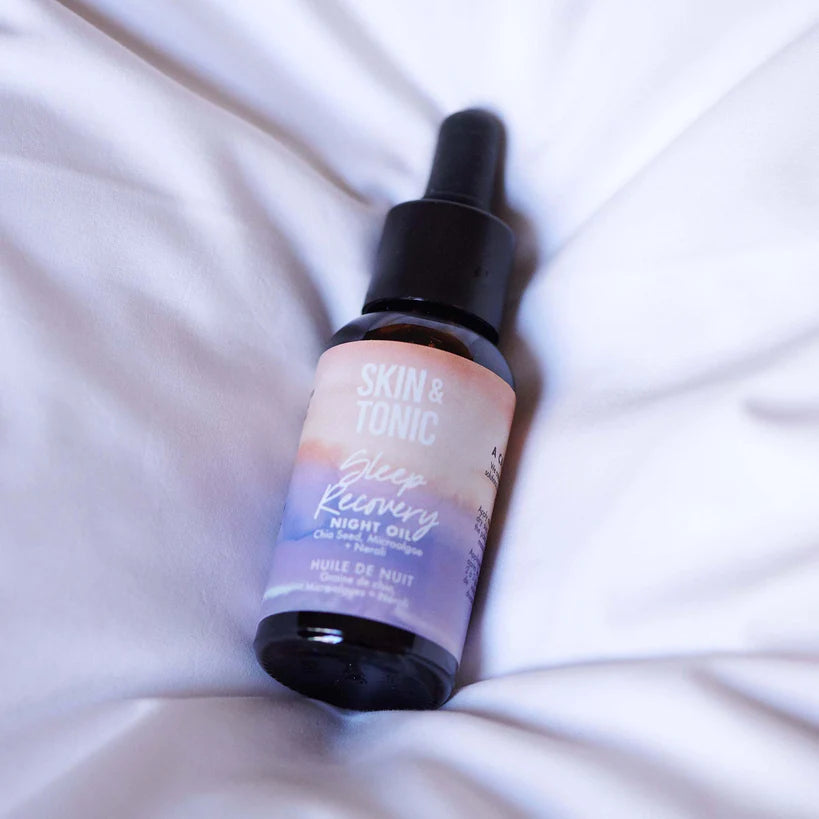 Skin & Tonic Sleep Recovery kasvoöljy; pullo mustalla tiputinkorkilla lepää sileillä valkoisilla lakanoilla; lasipullo lieriön muotoinen, mattapintainen ja pastellisävyinen etiketti; teksti "Skin & Tonic Sleep Recovery Night Oil" selvästi näkyvissä.