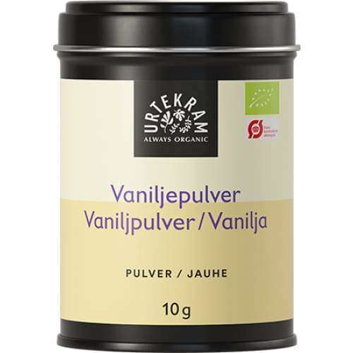 Urtekram Luomu Vaniljajauhe; musta, suorakulmainen metallirasia mattapinnalla tekstillä "Urtekram Always Organic", sisältää 10 g vaniljajauhetta; kerman- ja vaaleankeltainen paperietiketti kiertyy suurimman osan purkista, näyttäen mustaa groteskitekstiä kolmella kielellä ja luomusertifiointilogoja; lähikuva yhtenäistä valkoista taustaa vasten; ei ihmisiä tai käsiä.