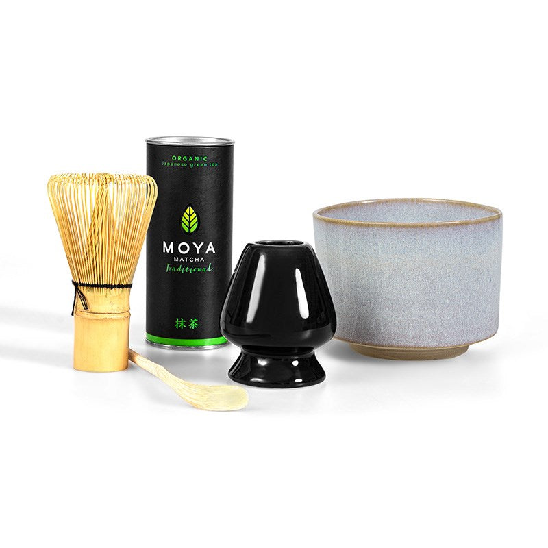 Moya Matcha Traditional Seremoniapakkaus; matchateesetti sisältäen luonnonvärisen bambuvispilän, kiiltäväpintaisen mustan keraamisen vispiläalustan, pyöreäreunaisen keraamisen kulhon, pienen premium Moya-matchatölkin vihreä-valkoisella pakkauksella ja yksinkertaisella sans-serif-typografialla sekä sileän bambuisen mittalusikan; kaikki tasaisesti aseteltuna valkoiselle pinnalle ylhäältä kuvattuna.