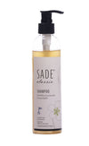 A clear bottle of SADE classic shampoo with a black pump, featuring Finnish text and a simple floral illustration on the label. The bottle is cylindrical, transparent, and has a glossy finish. The label uses clean sans-serif typography in black. Product stands alone against a plain light background, no people or actions shown.