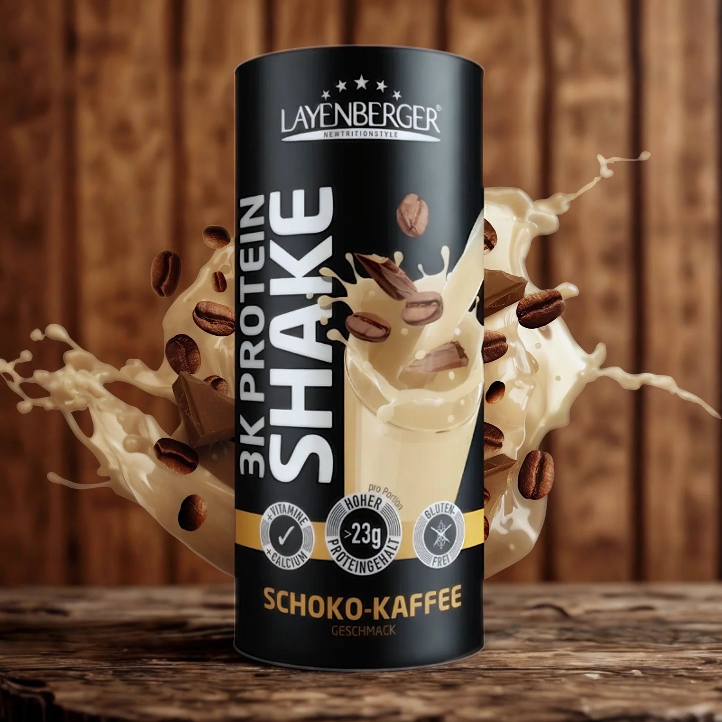 3K Protein Shake Chocolate Coffee; Layenberger 3K Protein Shake -tölkki Schoko-Kaffee-makuisena pystyssä, ympärillä kermaisia proteiinipitoisia nesteroiskeita, suklaanpaloja ja kahvipapuja rustiikkia puutaustaa vasten; tölkki sylinterin muotoinen mattapinnalla, lihavoitu valkoinen ja ruskea kirjasin; ei ihmisiä tai käsiä kuvassa.