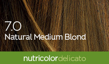 Biokap Nutricolor Delicato Kestoväri; lähikuva keskivaaleasta tukasta tekstillä 7.0 Natural Medium Blond päällekkäin; kuvassa yhtenäinen vihreä palkki alareunassa valkoisella groteskitekstillä ”nutricolor delicato for vibrant, gentle color”; ei pakkausta, ihmisiä tai taustaelementtejä näkyvissä; kuva tiukasti rajattu vain tukkaan ja tekstiin.
