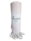 AAMU Hamam Kylpypyyhe; kääritty vaaleanpunainen puuvillapyyhe valkoisin hapsuin päissä; pyyhe kääritty etiketillä, jossa lukee "Aanu" ja "100% cotton" suomeksi selkeällä sans-serif-fontilla; materiaalin pinta mattainen ja tekstiilimäinen; ei ihmisiä tai käsiä näkyvissä; tausta yksinkertainen ja siisti; keskikuva lähietäisyydeltä.