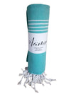 A rolled turquoise towel with white fringe and horizontal stripes, featuring the Aamu label on the wrapper. Cotton textile has a matte finish. The towel is tightly rolled into a cylinder. Label shows “Aamu” in simple sans-serif font; text is centered and black on white. Image background is plain and light colored, no other objects or people visible. Shot is a well-lit studio close-up from above.