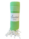 A green towel with white stripes, rolled up and secured with a white label reading “Aanu.” The towel is made of fabric with soft, white fringed ends. Matte surface finish. No packaging aside from the label. Bold, sans-serif font on the label. Shot on a plain background, no people or hands visible.