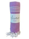 A rolled lavender peshtemal towel with white decorative stripes, fringed ends, and an Aamu label. The towel is made of a flat-weave fabric with a matte finish. The Aamu label is sewn onto one end and displays the brand name in sans-serif font. The product is photographed on a plain, light background and no packaging or people are visible.