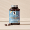 Active Magnesium Gummies Sitraatti; pullo New Nordic Active Magnesium Citrate Vegan Gummies seisoo beigellä pinnalla, kaksi magnesiumpurutablettia vieressä; pullo lieriömäinen muovia valkoisella kannella; etiketti sininen, näyttää luettavaa valkoista ja oranssia tekstiä groteskifontilla; ei ihmisiä tai käsiä; asetelma yksinkertainen ilman muita esineitä kuvassa.
