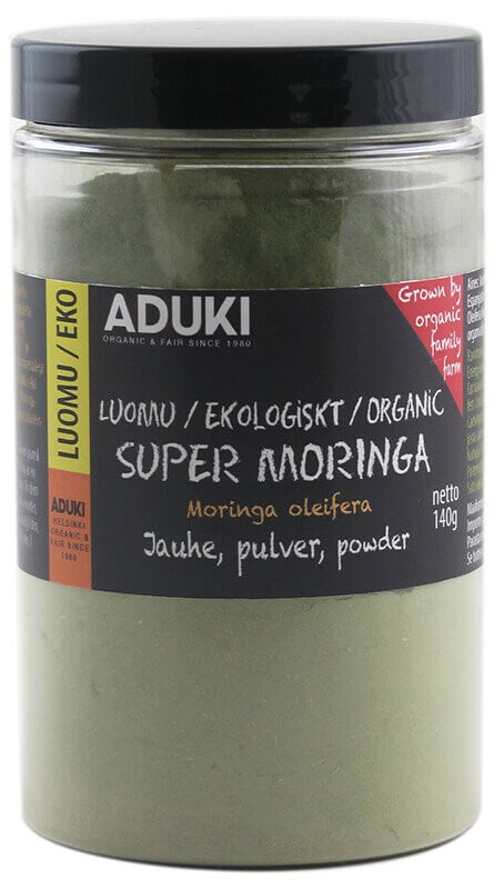 Aduki Luomu Moringajauhe, 140 g, kirkkaassa muovipurkissa; purkki sylinterimäinen ja täynnä hienoa vihreää jauhetta; musta-keltaisessa etiketissä lohkokirjaimia, monikielistä tekstiä sekä punainen huomiomerkintä luomutilan kasvatuksesta; etiketti keskitetty purkin rungolle; tausta valkoinen ja tasaisesti valaistu.