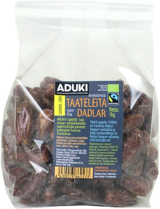 Aduki Luomu Kuivattu Taateli; kirkas muovipussi Aduki-merkkisiä kivettömiä taateleita etikettein suomeksi ja ruotsiksi, näyttäen sertifiointilogot ja tuotetiedot; 1 kg pussi näyttää viivakoodin alaosassa; pussi suorakaiteen muotoinen, kiiltävää läpinäkyvää materiaalia, ruskeita taateleita näkyvissä sisällä, valkoinen tausta; luettava teksti painettu mustana etikettiosioihin; ei ihmisiä tai käsiä; kuvattu edestä.