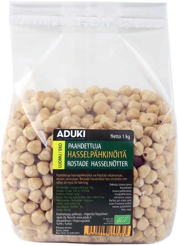 Aduki Luomu Paahdettu Hasselpähkinä; kirkas muovipussi täynnä paahdettuja hasselpähkinöitä; suorakaiteen muotoinen, läpinäkyvä pakkaus kiiltäväpinnalla; etiketti musta-valkoinen lihavoidulla groteskifontilla ADUKI; muut näkyvät tiedot suomeksi ja ruotsiksi, vihreä ekomerkki ja nettopaino 1 kg; neutraali tausta; ei ihmisiä tai käsiä näkyvissä.