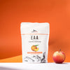 AlpenPower EAA Peach Iced Tea; valkoinen matta muovipussi tekstillä ”AlpenPower EAA Amino Acids” seisoo pystyssä; pakkauksessa painettu persikkakuvitus ja selkeä musta groteskiteksti; tuore kokonainen persikka aseteltuna pussin viereen; molemmat esineet oranssilla tasaisella pinnalla; ei ihmisiä tai toimintaa kuvassa.