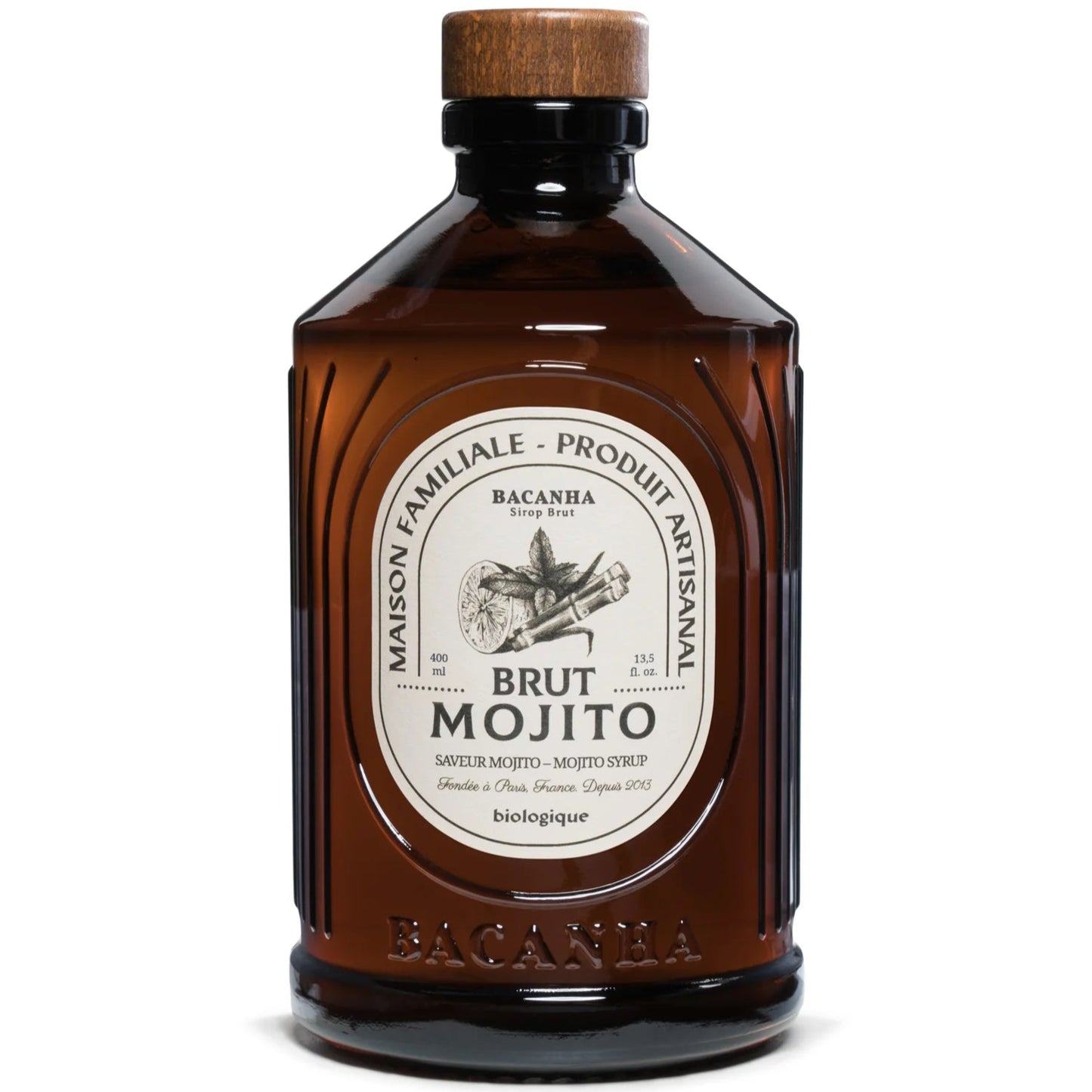 Bacanha Luomu Mojitosiirappi; ruskea lasipullo, merkitty Brut Mojito, valmistaja Bacanha, suorakulmainen valkoinen ja kultainen etiketti mustalla groteskitekstillä sekä kiiltävä musta kierrekorkki; etiketissä lisää ranskankielistä tekstiä, tietoa luonnollisista ainesosista ja tuotetiedoista; kuva keskitetty vaaleaa, yksivärista taustaa vasten, ei ihmisiä tai käsiä näkyvissä.