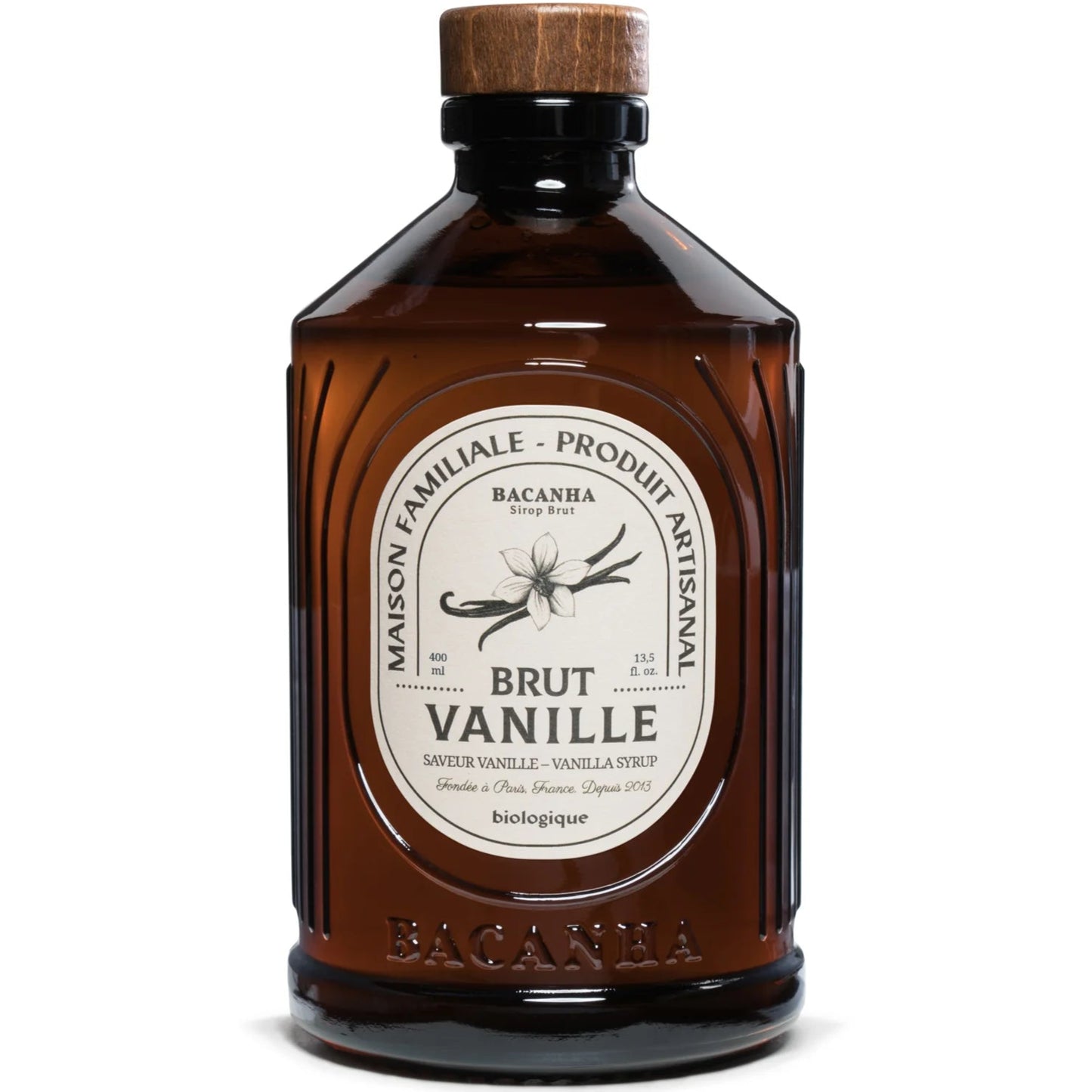 Bacanha Luomu Vaniljasiirappi; ruskea lasipullo, merkitty Brut Vanille -vaniljasiirappi, valmistaja Bacanha, puinen korkki ja koristeellinen valkoinen ja kultainen etiketti vaniljankukkakuvituksella ja sanalla "vanilla"; pullo on sylinterinmuotoinen; pääteksti lihavalla antiikvatypografialla; pinta kiiltävä; tuote kuvattu vaaleaa taustaa vasten, ei ihmisiä, käsiä tai muita esineitä näkyvissä.