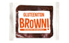 Balviten Gluteeniton Brownie; pakattu gluteeniton suklaabrownie kirkkaassa suorakulmaisessa muovikääreessä; etiketissä lukee GLUTEENITON BROWN! lihavalla oranssilla ja alla SUKLAALEIVOS SUKLAAPALOILLA valkoisin kirjaimin oranssia taustaa vasten; etiketti on kiiltäväpintainen groteskityypografialla; ei ihmisiä tai käsiä näkyvissä; tausta vaalea.