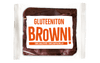 Balviten Gluteeniton Brownie; pakattu gluteeniton suklaabrownie kirkkaassa suorakulmaisessa muovikääreessä; etiketissä lukee GLUTEENITON BROWN! lihavalla oranssilla ja alla SUKLAALEIVOS SUKLAAPALOILLA valkoisin kirjaimin oranssia taustaa vasten; etiketti on kiiltäväpintainen groteskityypografialla; ei ihmisiä tai käsiä näkyvissä; tausta vaalea.