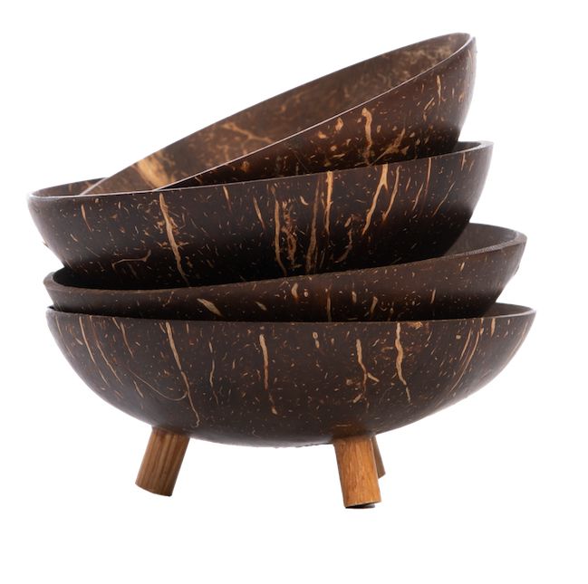 Four stacked, round brown coconut shell bowls with a natural, marbled texture are supported by three short wooden legs and set against a plain white background. The bowls have a matte finish and distinctive light and dark streaking typical of coconut shell. No labels or visible text. No packaging present. No people or hands in frame. The photograph is taken from a front angle with neutral lighting.