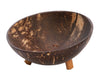 A bowl crafted from a coconut shell with a natural, textured surface, round in shape, and supported by three short cylindrical wooden legs. The finish is matte with visible grain patterns unique to coconut shells. There is no packaging or label text present. The item is photographed against a white background. A bowl crafted from a coconut shell with a natural, textured surface, sitting on three short wooden legs against a white background—an eco-friendly addition to your décor.