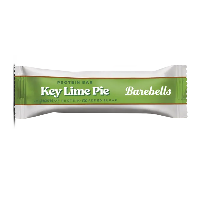 Barebells Key Lime Pie Proteiinipatukka; Barebells-proteiinipatukka Key Lime Pie -maussa, käärittynä eloisaan valkoiseen ja vihreään pakkaukseen kultaisin reunuksin, etupuolella Key Lime Pie- ja Barebells-merkinnät; pakkaus on kiiltävä, suorakulmainen ja suljettu molemmista päistä; typografia lihavaa ja groteskia pääteksteissä; tausta valkoinen; ei ihmisiä tai käsiä näkyvissä, tuote esillä keskitetyssä tasokuvassa.