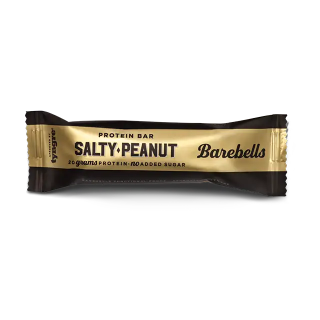 Barebells Salty Peanut Proteiinipatukka; kultaisessa ja mustassa kääreessä oleva Barebells-proteiinipatukka suolaisella maapähkinän maulla, tekstissä 20 grammaa proteiinia ja ei lisättyä sokeria valkoisella taustalla; pakkaus kiiltopinnalla lihavoidulla valkoisella ja kultaisella kirjasimella; patukka suorakulmainen ja aseteltu vaakasuoraan kuvan keskelle; ei ihmisiä tai esineitä.
