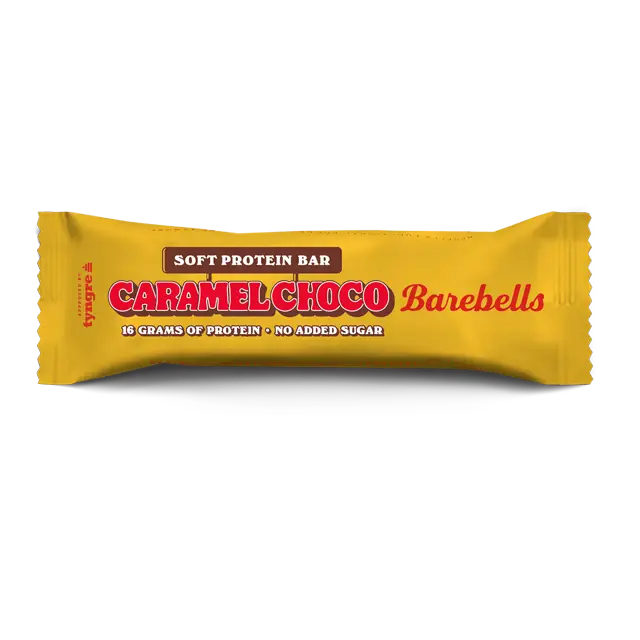Barebells Soft Caramel Choco Proteiinipatukka; keltainen Barebells-proteiinipatukan kääre nimellä Caramel Choco, teksti kertoo 16 grammaa proteiinia, ei lisättyä sokeria ja pehmeän proteiinipatukan rakenteen; pakkaus suorakaiteen muotoinen kiiltäväpinnalla ja rypytetyin reunoin; teksti lihavoitua groteskia mustavalkoisena; pinnassa vain painettua grafiikkaa, ei näkyvää tuotetta tai avattua pakkausta; vaalea tausta, ei ihmisiä tai käsiä.