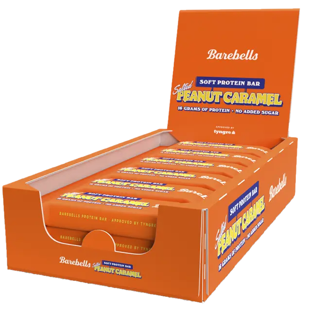 Barebells Soft Salted Peanut Caramel Proteiinipatukka; laatikko Barebells-pehmeitä proteiinipatukoita, maku suolainen maapähkinäkaramelli, useita yksittäin käärittyjä patukoita eloisan oranssin pakkauksen sisällä; laatikko suorakaiteen muotoinen kiiltäväpinnalla, lihavoitua valkoista ja ruskeaa typografiaa; tuotenimi ja maku selkeästi näkyvissä etuosassa; neutraali alusta, ei ihmisiä tai toimintaa; kuvattu yläviistosta.