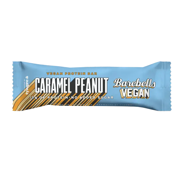 Barebells Vegan Caramel Peanut Proteiinipatukka; sininen Barebells Vegan Caramel Peanut -proteiinipatukan kääre kultaisin ja valkoisin tekstein, esittelee kasviperäisiä ainesosia, 15 g proteiinia ja ei lisättyä sokeria; kääre suorakaiteen muotoinen kierretyin reunoin ja mattapintainen; teksti tikkukirjasimella lihavoituna ja tavallisena painona; tuote lepää tasaisella alustalla, ei ihmisiä tai muita esineitä kuvassa.