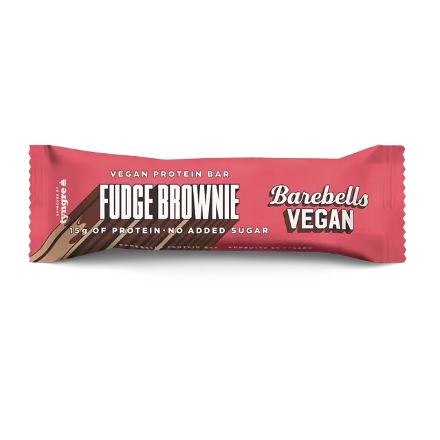 Barebells Vegan Fudge Brownie Proteiinipatukka; Barebells Vegan Fudge Brownie -proteiinipatukka vaaleanpunaisessa, kiiltävässä muovipakkauksessa valkoista taustaa vasten; kääre on suorakulmainen suljetuin päin; etiketissä lihavaa groteskitekstiä ”15g of protein” ja ”no added sugar”; ei ihmisiä tai rekvisiittaa, vain tuote keskitettynä kuvaan.