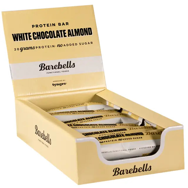 Barebells White Chocolate Almond Proteiinipatukka; keltainen Barebells White Chocolate Almond -proteiinipatukkarasia avoimena, näyttää yksittäin käärittyjä korkean proteiinipitoisuuden patukoita; rasia suorakulmainen mattapinnalla, valkoista ja ruskeaa lihavoitua groteskitekstiä; luettavassa tekstissä ”20 grams of protein” ja ”no added sugar”; rasia tasaisella pinnalla, ei ihmisiä tai käsiä kuvassa.