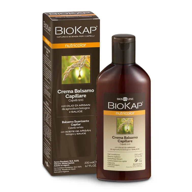 Biokap Nutricolor Conditioner for Dyed Hair; pullo BioKap Nutricolor Crema Balsamo Capillare -hoitoainetta värjätylle tukalle sekä sen vähittäismyyntirasia; sekä pullo että rasia tummanruskein taustoin oranssein korostuksin, mattapinta ja suorakulmainen muoto; kuvia vehnäntähkistä ja argaanipähkinöistä pakkauksessa; valkoinen groteskiteksti näyttää brändinimen ja tuotetiedot; pakkaus pystyssä tasaista taustaa vasten studiokuvassa, ei ihmisiä tai käsiä.
