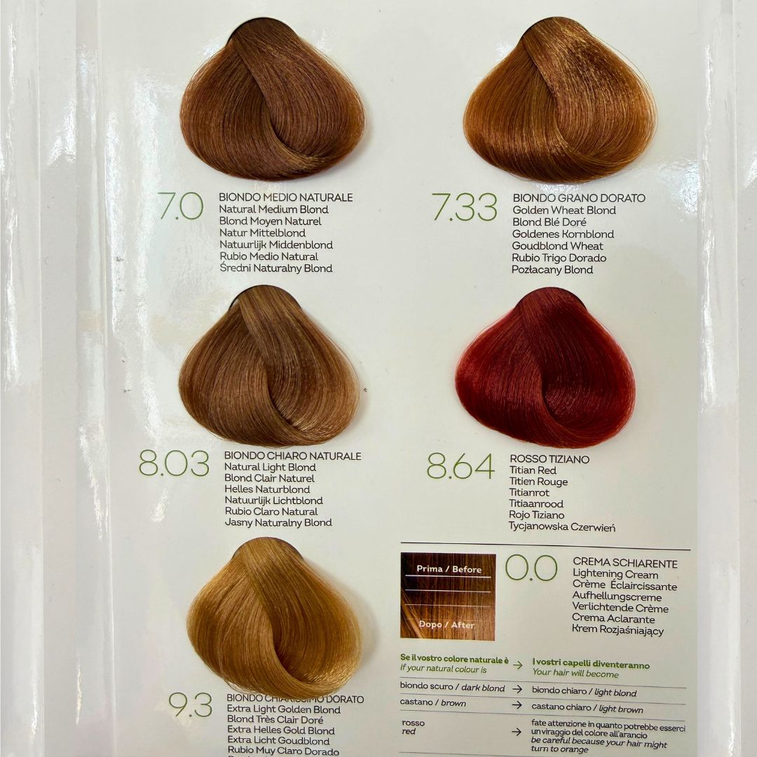 Biokap Nutricolor Delicato Kestoväri; kuusi hiusvärinäytettä merkittynä vaalean ja punaisen sävyissä, mukana neutraaleja, kultaisia ja titaanisävyjä; kukin näyte pieni hiusnäyte aseteltu yhteen riviin tasaiselle valkoiselle taustalle; näytteet kiiltäviä näkyvin tekstuurein; etiketit näyttävät numerot ja nimet italiaksi ja englanniksi groteskikirjasimella kunkin näytteen alla; ei pakkausta, ihmisiä tai käsiä näkyvissä.