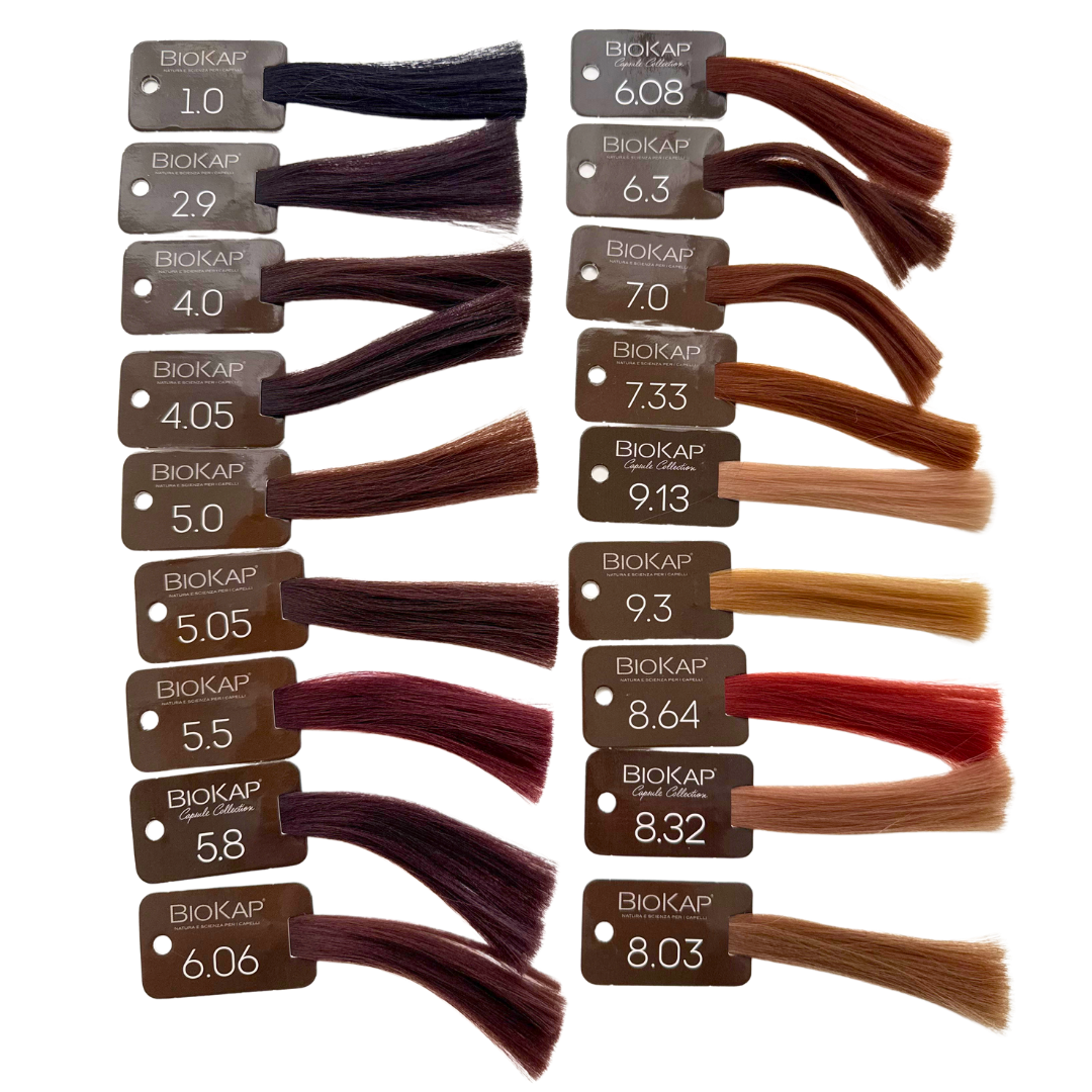 Biokap Nutricolor Delicato Kestoväri; numeroituja ja Biokap-brändättyjä hiusvärinäytteitä, sävyt mustasta ruskean, vaalean, kupari- ja punasävyihin, aseteltuna neljään pystyriviin valkoiselle taustalle; näytteet suorakulmaisia hiusnäytteitä kiinnitettynä tasaiseen mattaesittelykorttiin; etikettiteksti yksinkertaisella groteskikirjasimella; ei pakkausta tai ihmisiä näkyvissä, vain järjestetty kartta kuvassa.