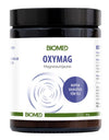 A black cylindrical plastic container of BIOMED Oxymag magnesium powder, matte finish, white wraparound label with blue and green sans-serif text, includes a spiral graphic element and a prominent blue circle with Finnish text indicating magnesium content. No people or hands visible. Product is isolated on a plain white background in a centered product shot.