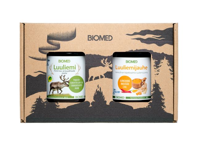 Two jars of Biomed brand broth powder are displayed in a matte cardboard box. The box has printed artwork showing trees and a reindeer silhouette in natural tones. Jars are cylindrical, with white caps and paper labels; “Biomed” is printed in bold sans serif font. The product name and some details are visible on the front labels. No people or hands appear.