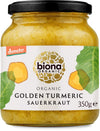 Biona Luomu Kurkumahapankaali, 350 g purkki luomukurkumahapankaalille pyöreässä lasipurkissa kultaisen metallikannen kera kiiltäväpinnalla; etusivun valkoisessa etiketissä graafinen kurkumajuuri kelta-oranssein sävyin ja vihreitä lehtiä, mukana Demeter-luomulogo; lihavoitu groteskiteksti tunnistaa tuotenimen ja painon; studiotausta yksinkertainen, ei ihmisiä eikä käsiä näkyvissä.