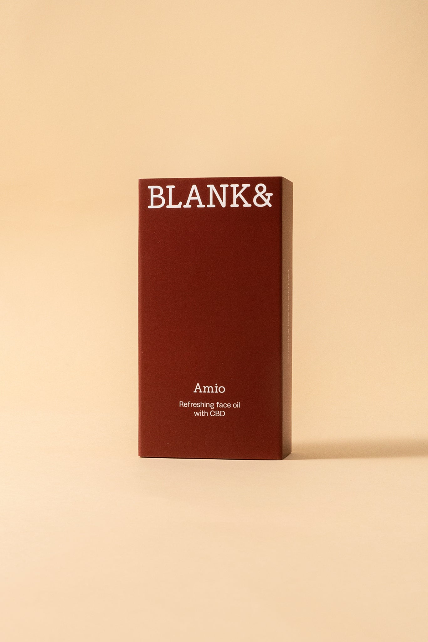 Blank& Amio Kasvoöljy; tummanpunainen rasia tekstillä BLANK& Amio Refreshing face oil with CBD seisoo pystyssä beigeä taustaa vasten korostaen tuotteen tyylikästä ulkoasua; rasia suorakulmainen terävin reunoin ja mattapinnalla; valkoinen suuraakkosin kirjoitettu teksti etupaneelissa; ei ihmisiä tai käsiä tässä suoraan edestä otetussa tuotekuvassa.