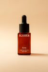 Blank& Evie Kasvoöljy; ruskea lasinen tippapullo tekstillä ”BLANK& Evie Calming face oil with CBD” seisoo pystyssä vaaleaa beigeä taustaa vasten; pullo sylinterin muotoinen pyöristetyin olkapäin ja mustalla tippakorkilla; etikettiteksti selkeää, mustaa groteskikirjasinta; lasin pinta kiiltävä ilman näkyvää kuviointia; ei ihmisiä tai käsiä kuvassa.