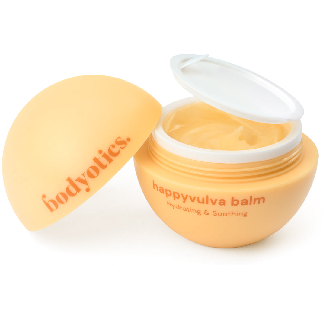 Bodyotics Happyvulva Balm; pyöreä persikanvärinen bodyotics happy vulva balm -purkki avoimena, sisällä näkyy kermaista, kosteuttavaa voidetta; pakkauksessa lukee oranssilla tekstillä ”hydrating & soothing”; purkin pinta matta ja materiaali muovia; etiketin kirjasin groteski ja selkeästi painettu; ei käsiä tai ihmisiä, tausta valkoinen ja pelkistetty.