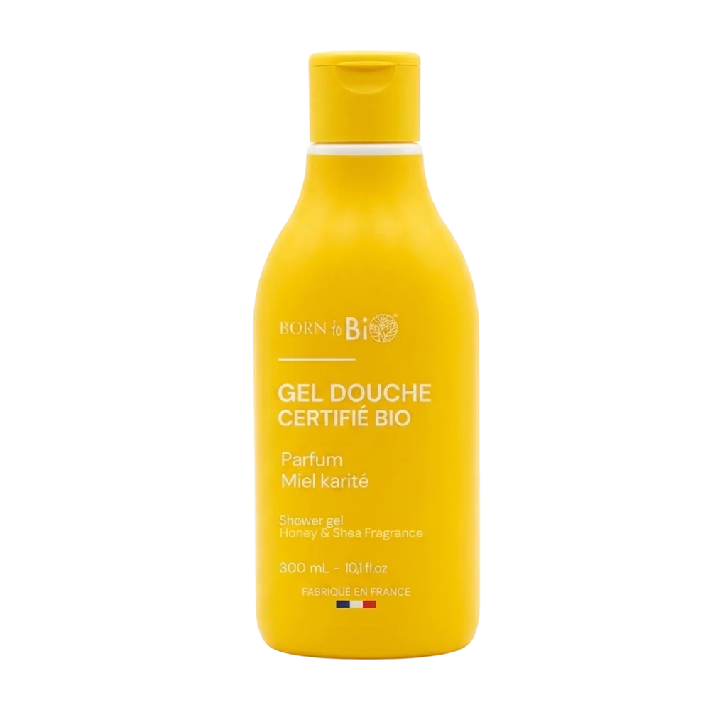 Keltainen Born to Bio -suihkugeelipullo, merkitty GEL DOUCHE CERTIFIÉ BIO, shea-hunajatuoksu, 300 ml, valmistettu Ranskassa, Ranskan lippu alaosassa; muovipullo pyöristetty mattapinnalla ja kierrekorkilla; etiketissä lihavoitua isokirjaimista typografiaa päätekstille; valkoinen tausta ilman näkyvää ympäristöä tai ihmisiä; kuva näyttää tuotteen kokonaisuudessaan edestä.