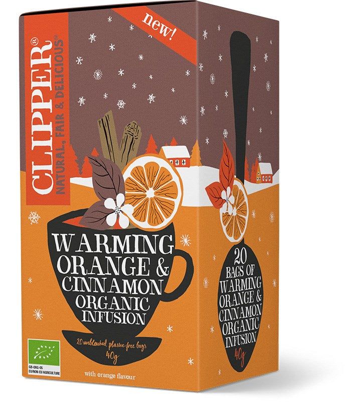 A box of Clipper organic tea, Warming Orange & Cinnamon flavor, featuring illustrations of a teacup, orange slices, cinnamon sticks, and a snowy village. The rectangular box is primarily orange with white and black accents and a matte finish. Serif and sans-serif typefaces are used on the packaging. The label states 20 bags of organic infusion. No people or hands visible; plain backdrop. The box contains 20 bags of organic infusion, blending zesty orange with aromatic cinnamon.